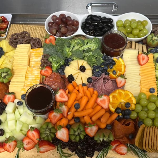 A large charcuterie board overflowing with cheeses, fruits, vegetables, meats, crackers, and dips.