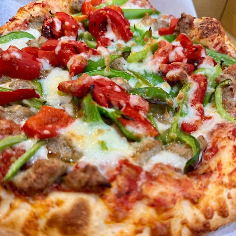 Close-up of a pizza with melted cheese, green bell peppers, red tomatoes, and sausage.