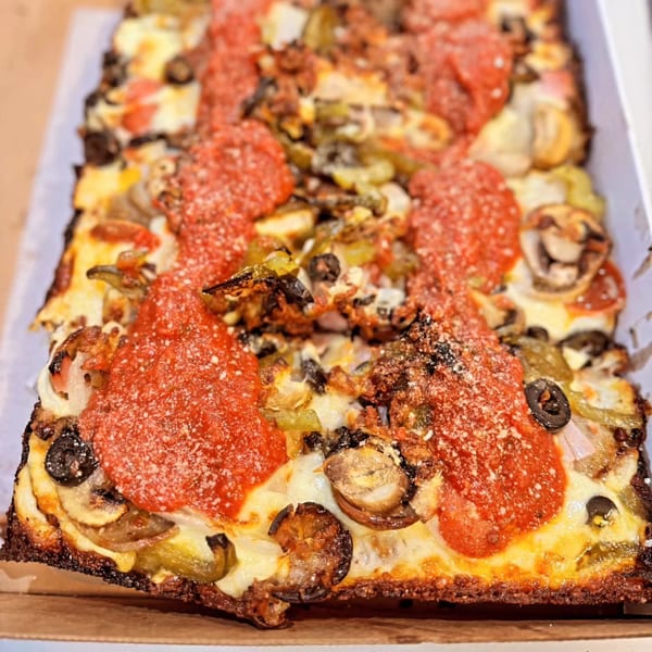A rectangular Detroit-style pizza with pepperoni, mushrooms, olives, and green peppers in a box.