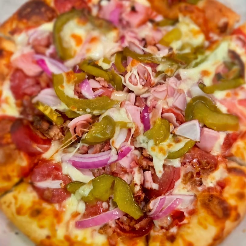 Close-up of a pizza topped with pepperoni, ham, red onions, and green peppers.